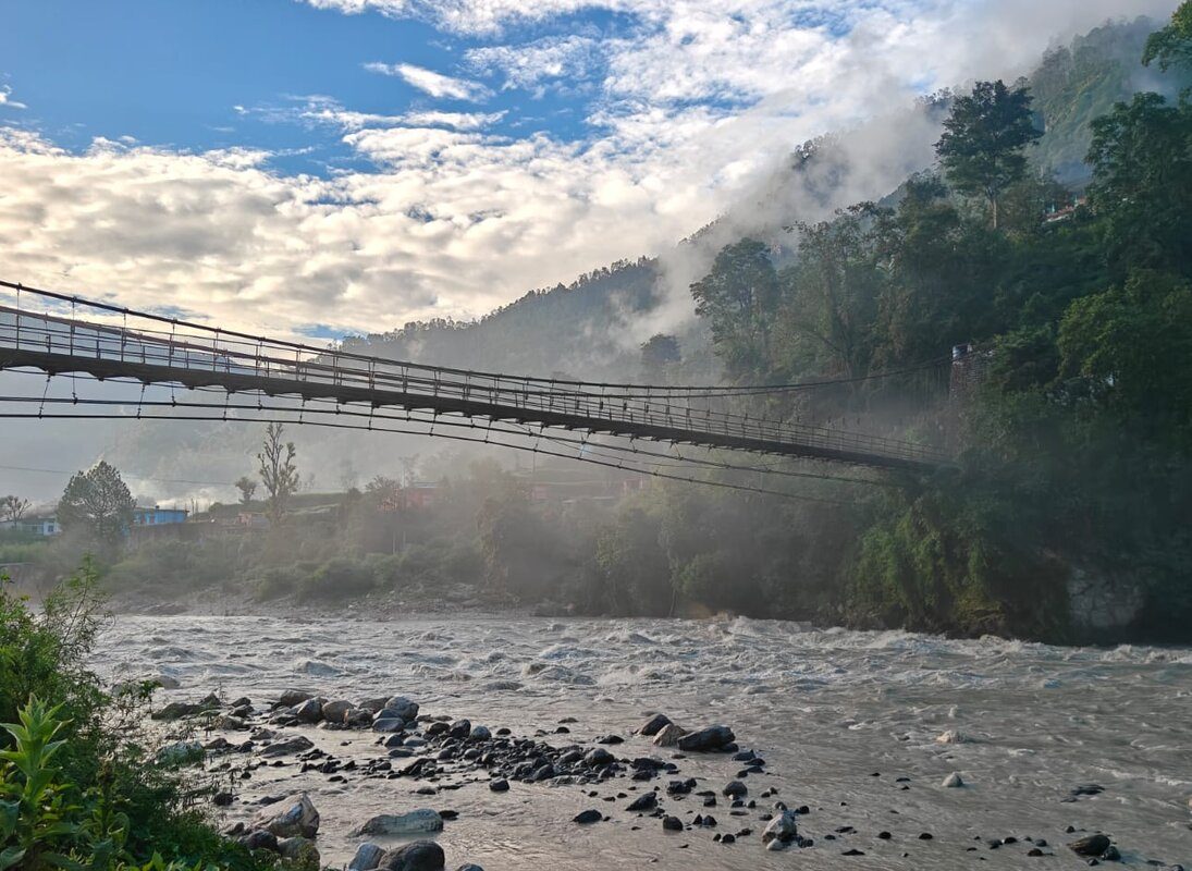 A misty suspension bridge crossing the Bhagirathi river at Uttarkashi, framed by forested hills