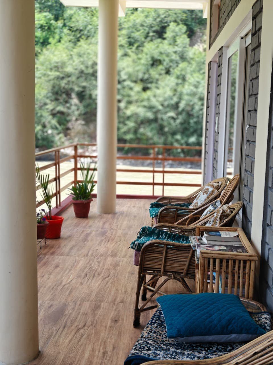 A quiet, empty veranda with reading chairs and books, overlooking greenery at Our Himalayan Home