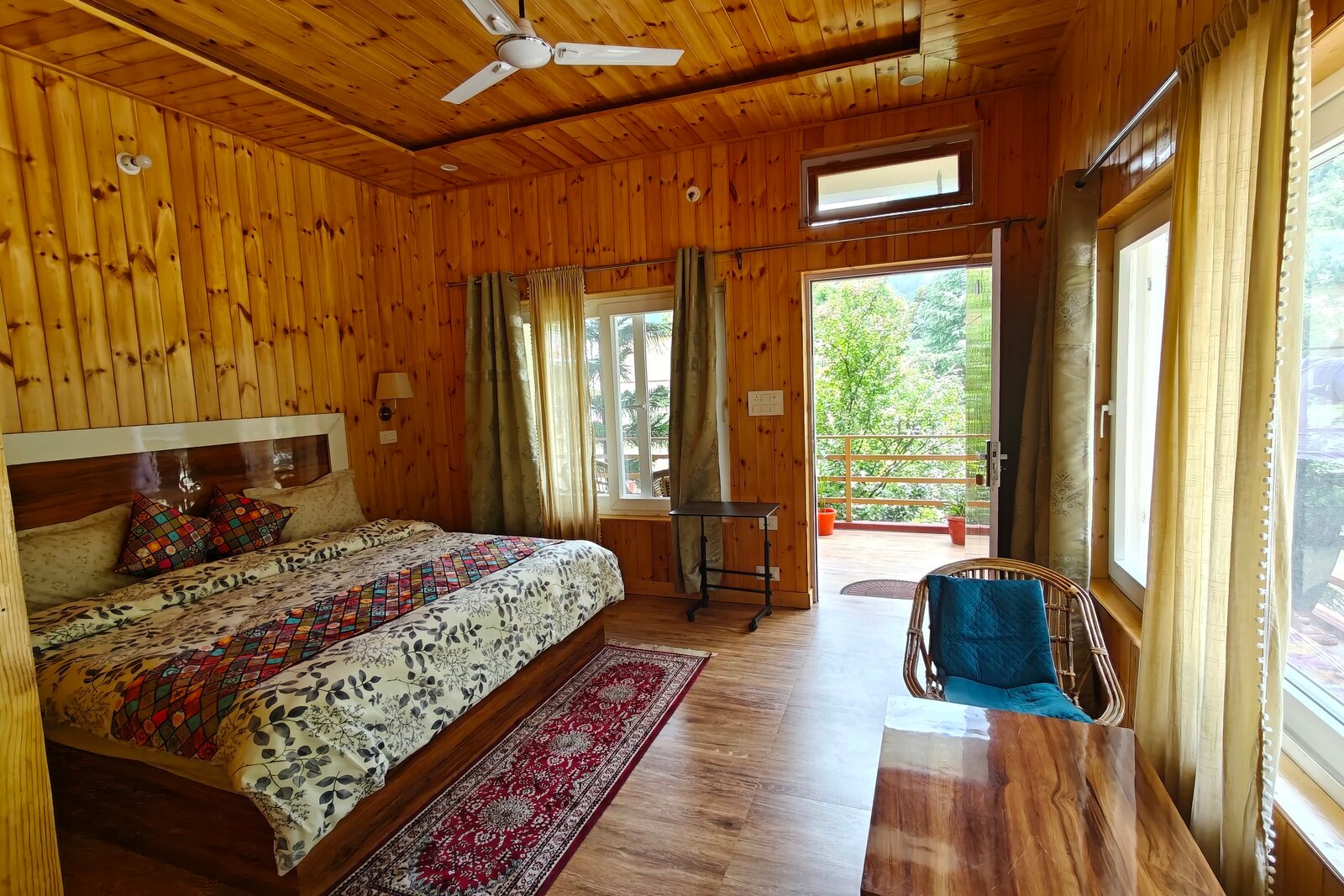 A wooden-panelled bedroom with a double bed and doors opening onto a balcony at the Uttarkashi venue