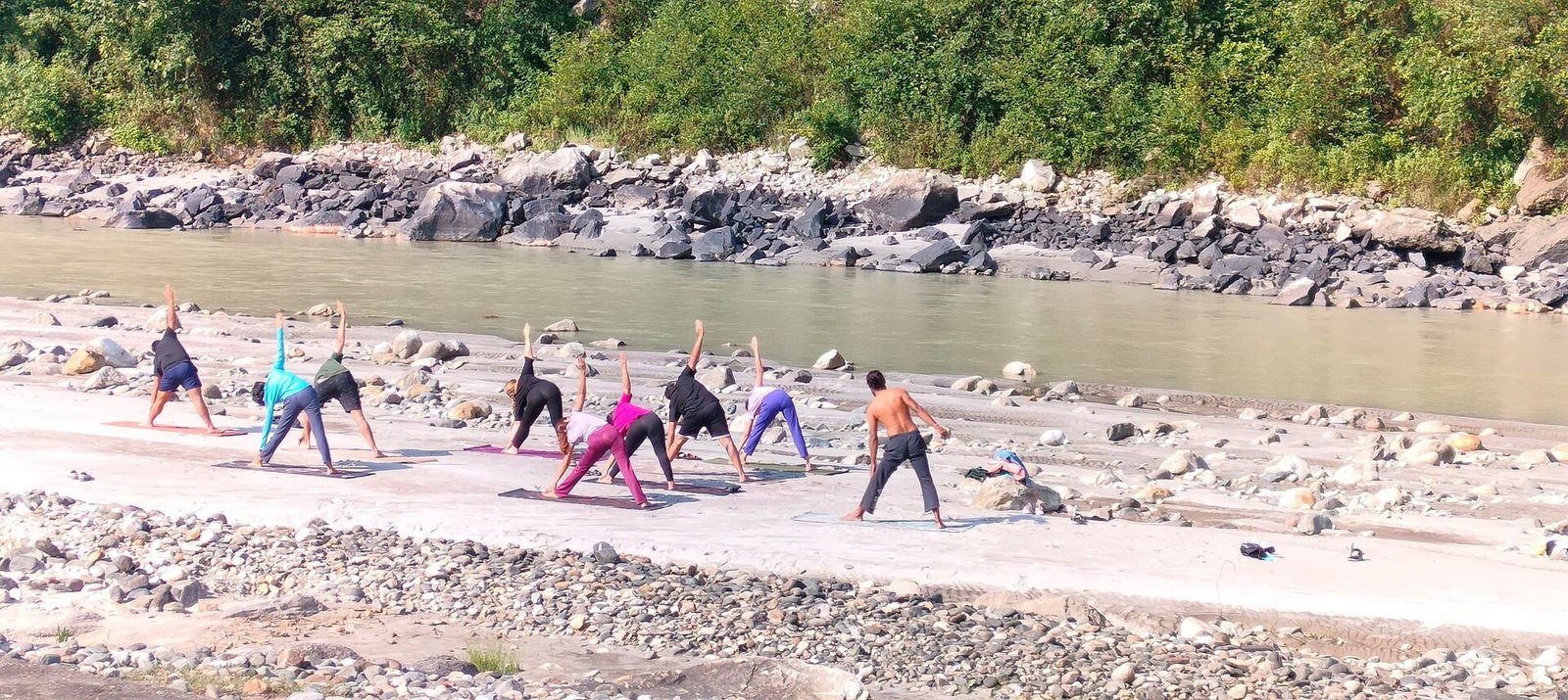 A group practising yoga together on the rocky bank of the Bhagirathi River near Uttarkashi